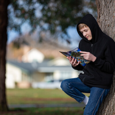 teen leaning against a tree reading a comic